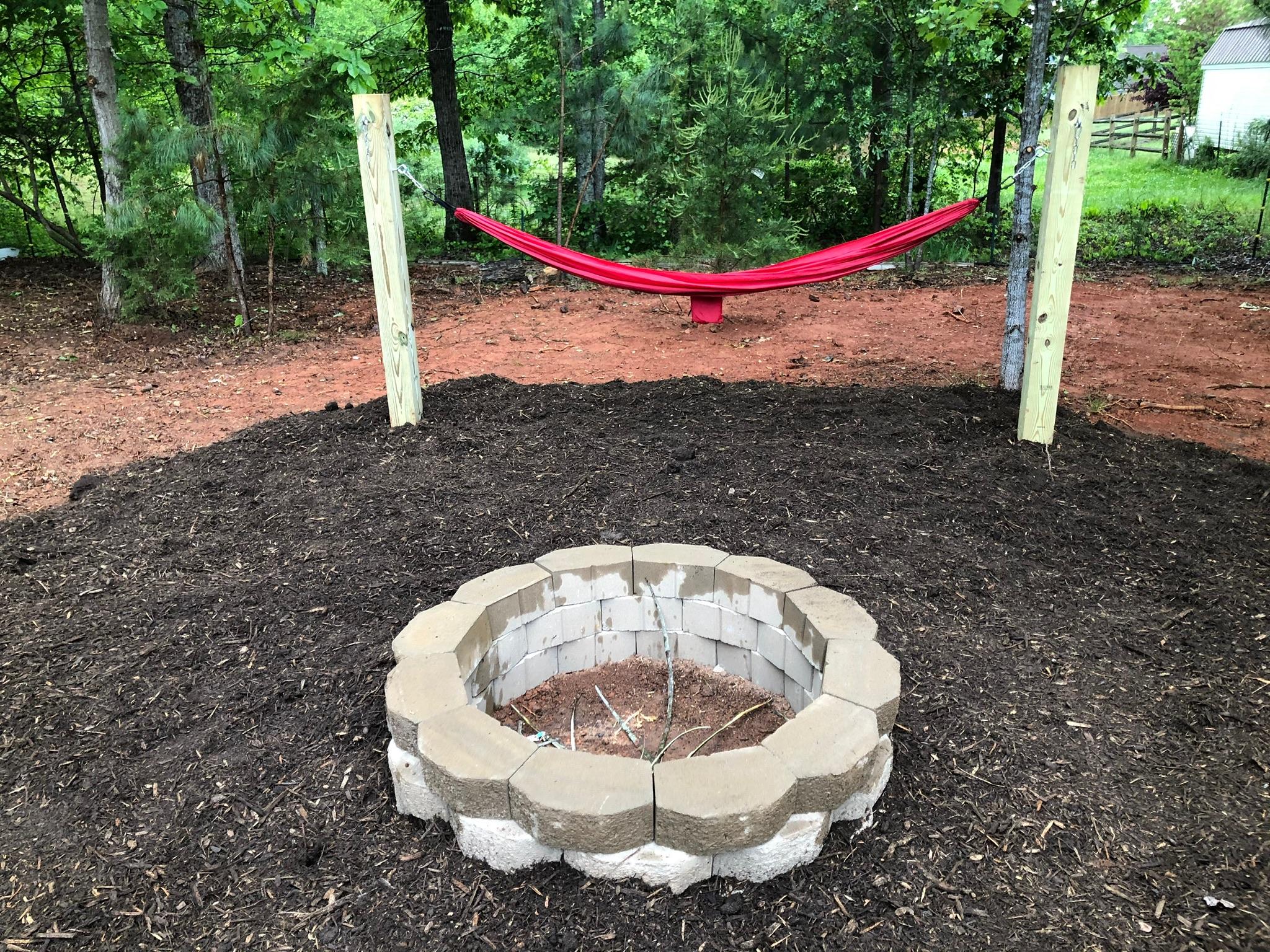 Round stone fire pit on a fresh mulched pad with hammock posts behind
