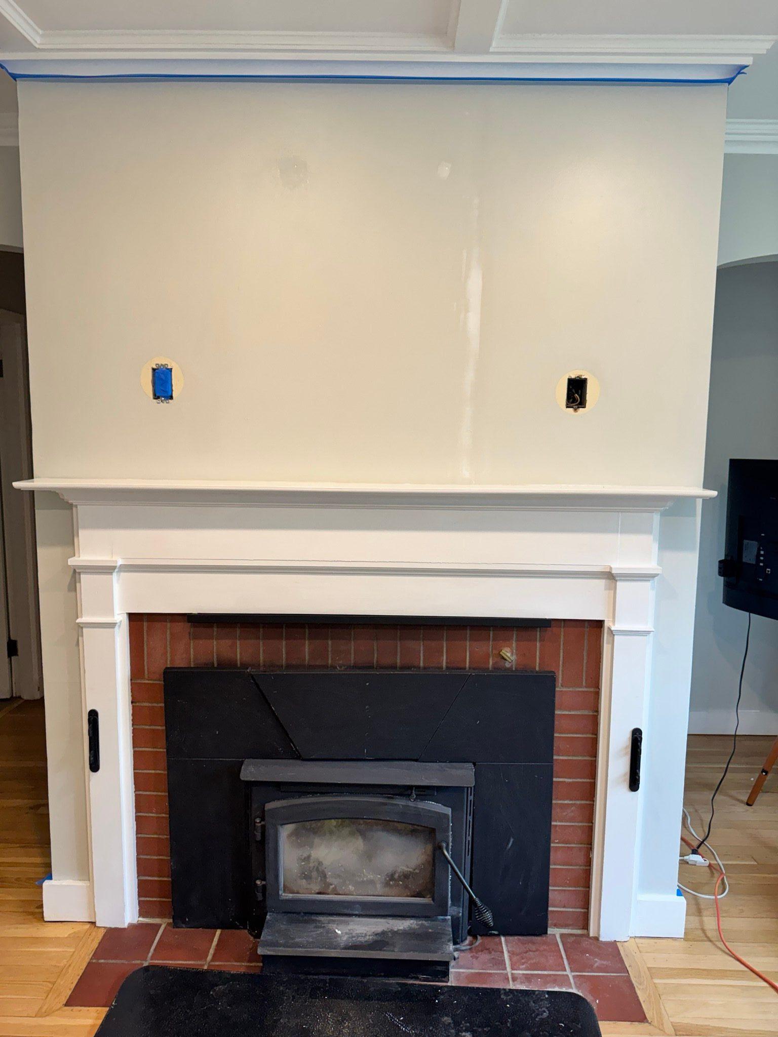 Fireplace mantle and surround freshly painted white with painter's tape still up and the wall above prepped, old light boxes converted to outlets for a media center