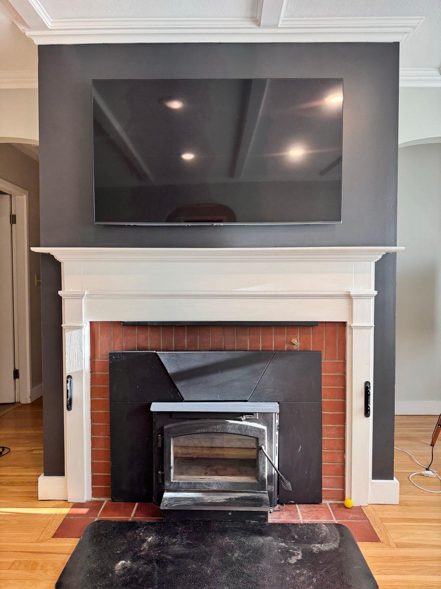 Finished fireplace with a dark charcoal accent wall and a flat-screen TV mounted flush above the white mantle, area cleaned up