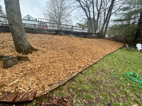 Large freshly mulched bed along a yard with a fence and patio chairs in the background