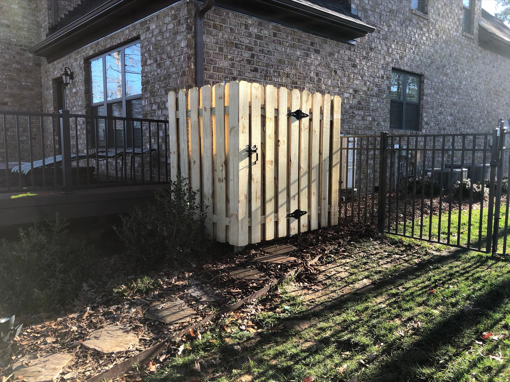 Custom cedar privacy screen built between an iron fence and a brick home to hide utilities